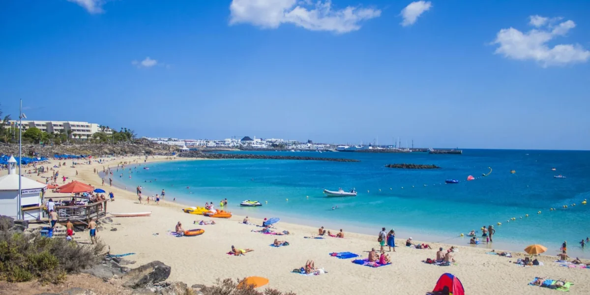 People enjoying a sunny day at Playa Blanca beach, Lanzarote with clear blue waters and golden sand.
