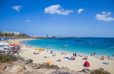 People enjoying a sunny day at Playa Blanca beach, Lanzarote with clear blue waters and golden sand.