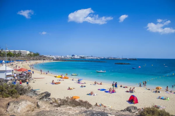 People enjoying a sunny day at Playa Blanca beach, Lanzarote with clear blue waters and golden sand.