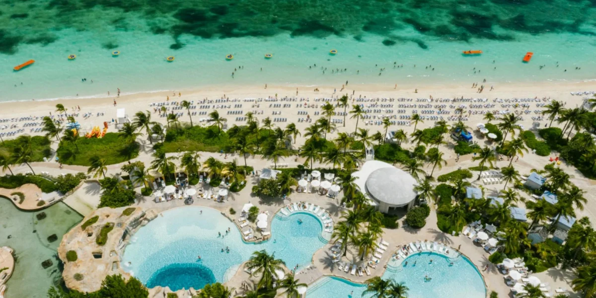 Aerial view of a luxury beachfront resort featuring swimming pools, palm trees, and a vibrant seaside.