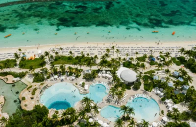 Aerial view of a luxury beachfront resort featuring swimming pools, palm trees, and a vibrant seaside.