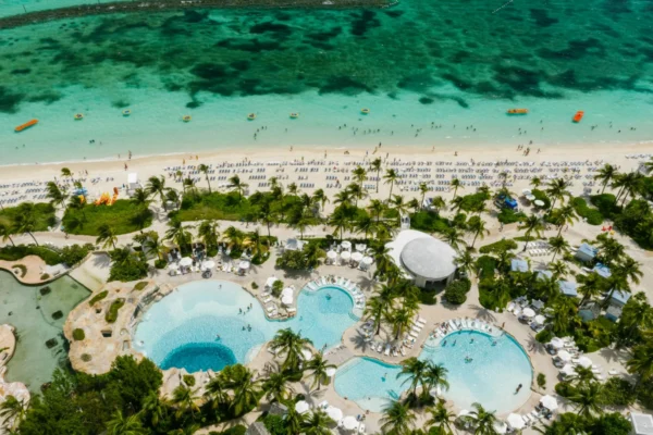 Aerial view of a luxury beachfront resort featuring swimming pools, palm trees, and a vibrant seaside.