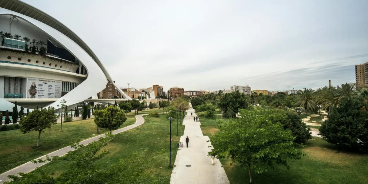 A spacious urban park with modern architecture and green walkways under a cloudy sky.