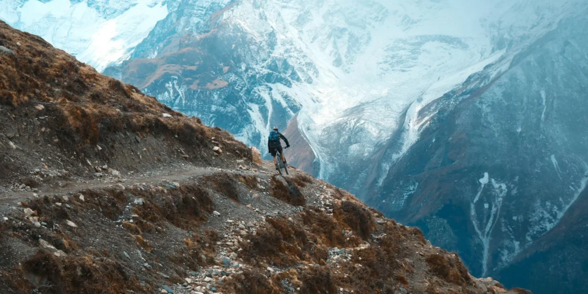 Cyclist on rugged mountain trail in Khangsar, Nepal with snow-capped peaks.
