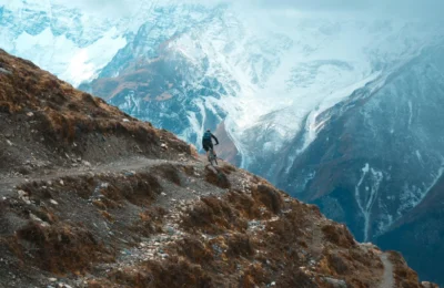 Cyclist on rugged mountain trail in Khangsar, Nepal with snow-capped peaks.