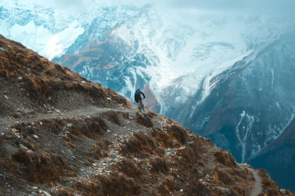 Cyclist on rugged mountain trail in Khangsar, Nepal with snow-capped peaks.