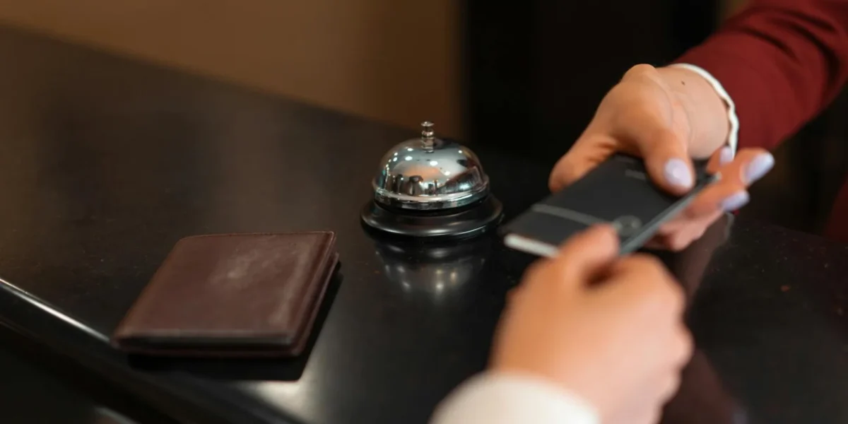 A close-up of a hotel check-in process with a smartphone and card transaction at the reception desk.