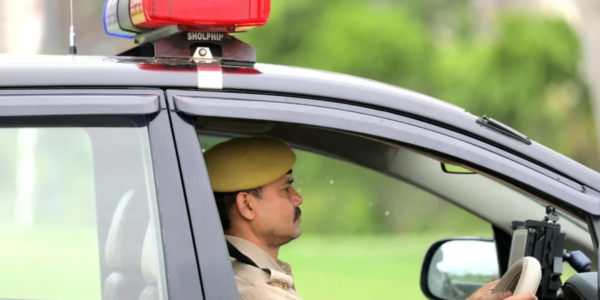 Side view of a police officer driving a patrol car with a visible siren outdoors.