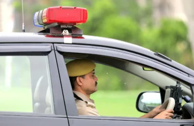 Side view of a police officer driving a patrol car with a visible siren outdoors.