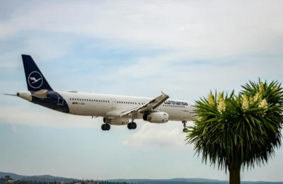 Lufthansa airplane approaching landing in Corfu, Greece with clear skies and palm trees.