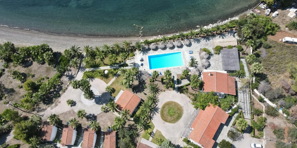 Aerial shot of a beautiful coastal resort in Loutraki, Greece, featuring a pool, beach, and lush surroundings.