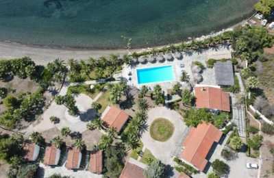 Aerial shot of a beautiful coastal resort in Loutraki, Greece, featuring a pool, beach, and lush surroundings.