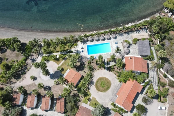 Aerial shot of a beautiful coastal resort in Loutraki, Greece, featuring a pool, beach, and lush surroundings.