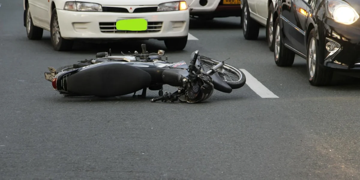 A motorcycle lies on a city road amidst traffic, indicating a recent accident.