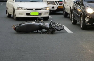A motorcycle lies on a city road amidst traffic, indicating a recent accident.