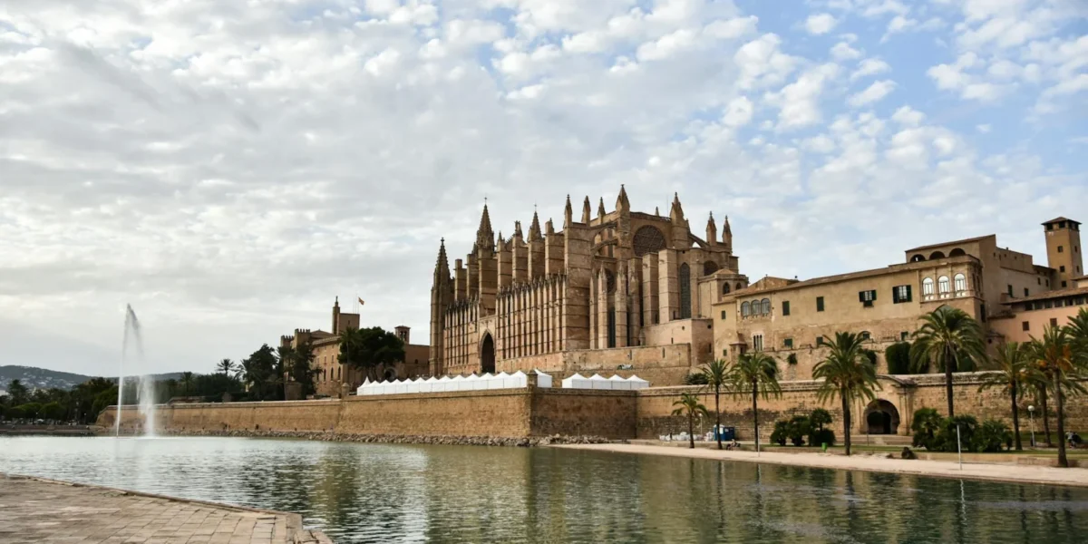 Stunning view of Cathedral de Mallorca by the tranquil waterfront under a cloudy sky.