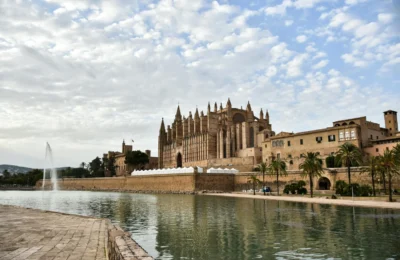 Stunning view of Cathedral de Mallorca by the tranquil waterfront under a cloudy sky.