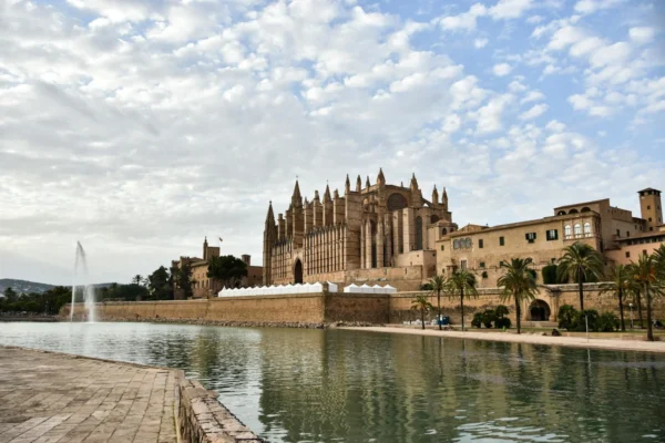 Stunning view of Cathedral de Mallorca by the tranquil waterfront under a cloudy sky.