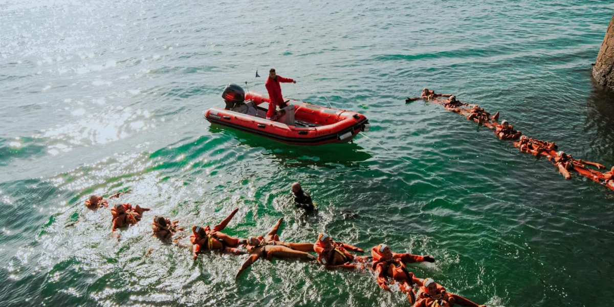 Aerial view of lifeguards in orange gear practicing rescue drills in the ocean.