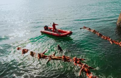 Aerial view of lifeguards in orange gear practicing rescue drills in the ocean.