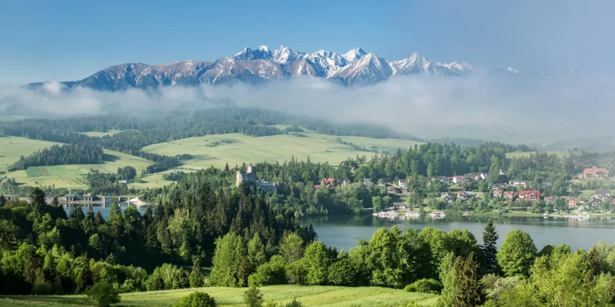 A breathtaking view of the Tatra Mountains enveloped in mist with a lush green landscape in the foreground.