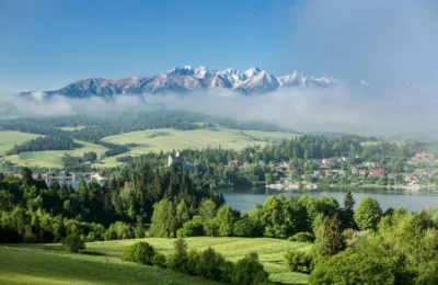 A breathtaking view of the Tatra Mountains enveloped in mist with a lush green landscape in the foreground.