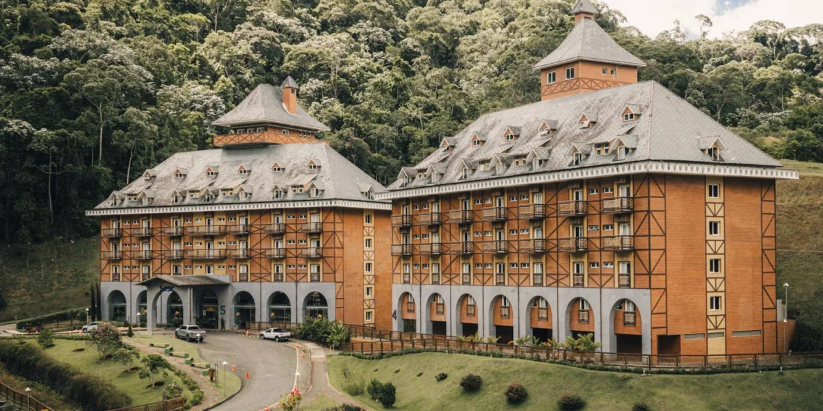 A picturesque Bavarian-style hotel surrounded by lush greenery and forest hillside.