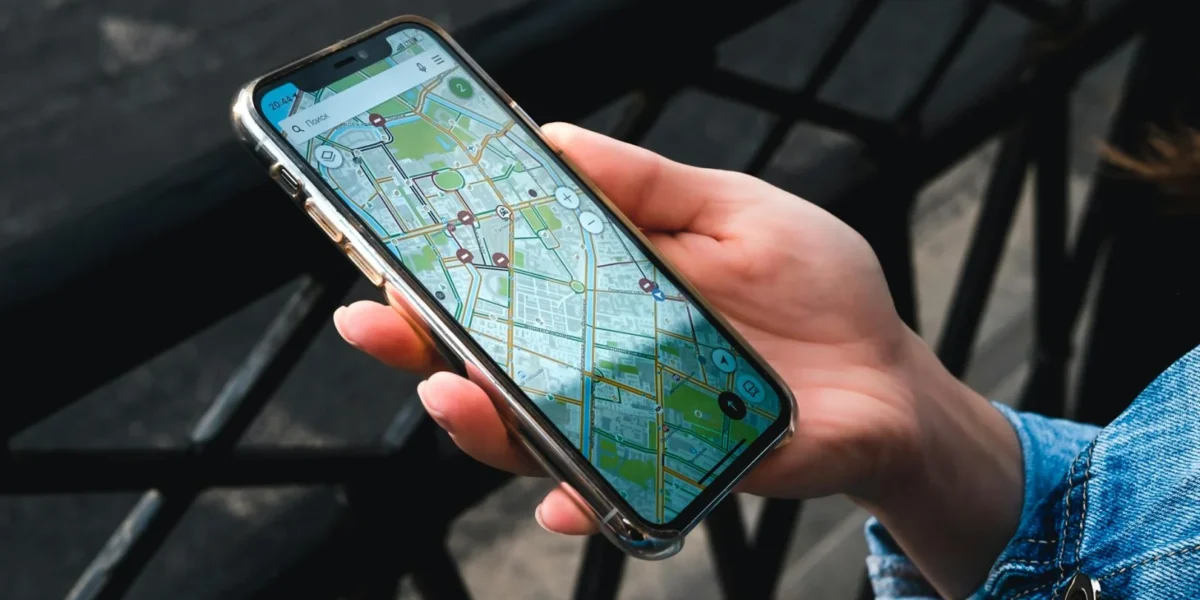 An outdoor close-up of a hand holding a smartphone displaying a map application.