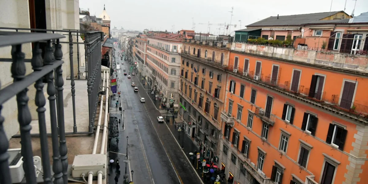 A rainy cityscape view of a Rome street, seen from a balcony, highlighting urban architecture.