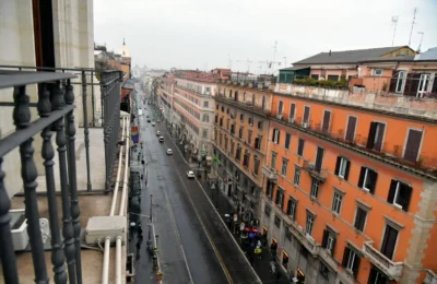 A rainy cityscape view of a Rome street, seen from a balcony, highlighting urban architecture.