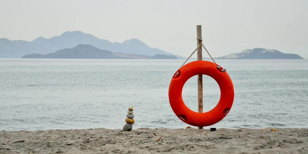 A tranquil beach in Kos, Greece, featuring a lifebuoy and rock cairn against a calm sea.