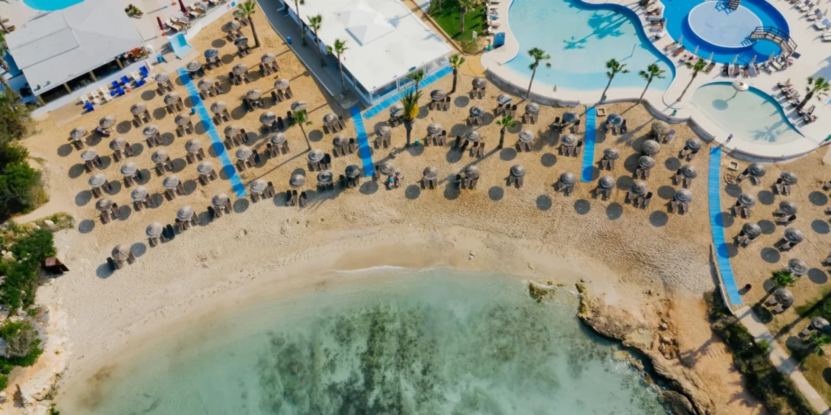 Aerial view of a tropical beach resort with pools and sun loungers, ideal for tourism.