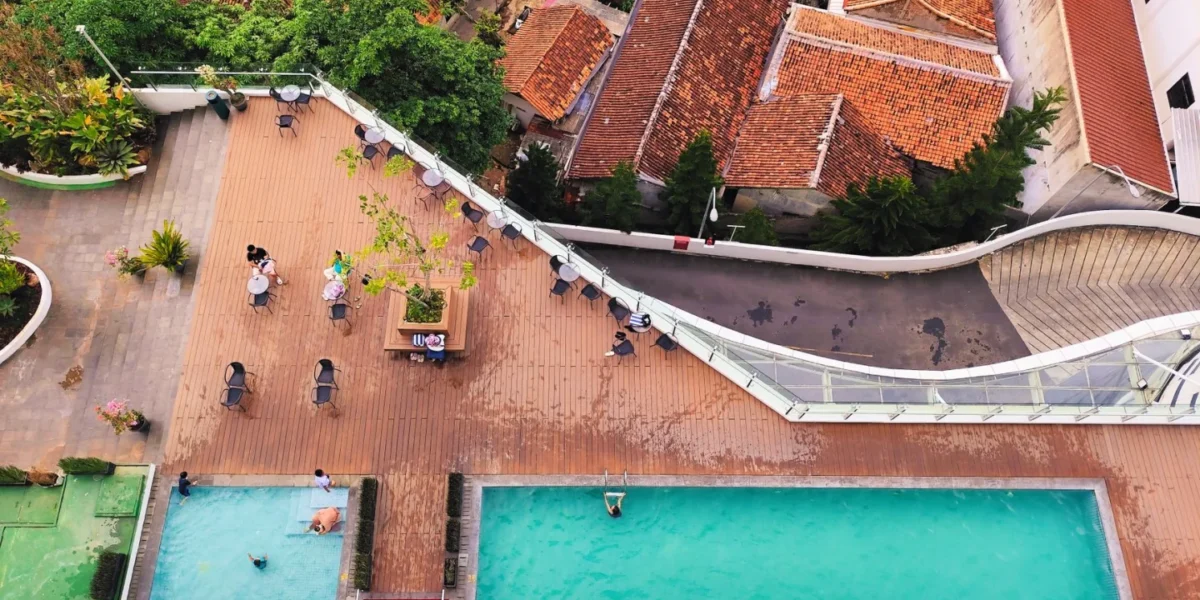 Aerial view of a rooftop pool area with swimmers and vibrant cityscape backdrop.