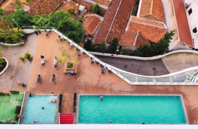 Aerial view of a rooftop pool area with swimmers and vibrant cityscape backdrop.