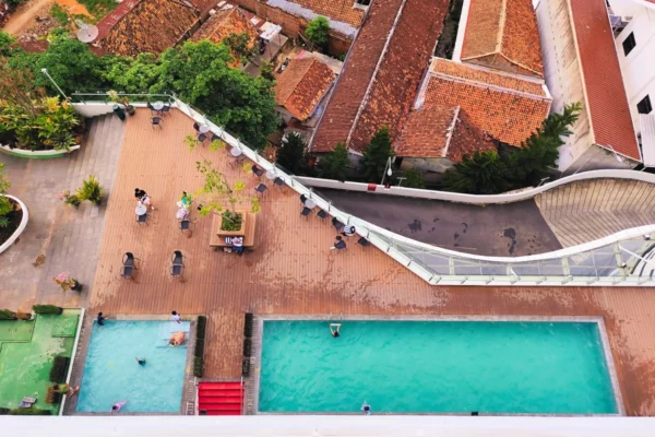 Aerial view of a rooftop pool area with swimmers and vibrant cityscape backdrop.
