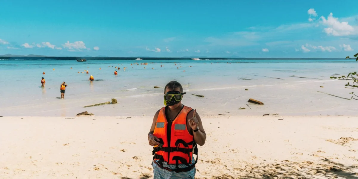 Person in snorkeling gear on a sunny beach in Krasom Subdistrict, Thailand.