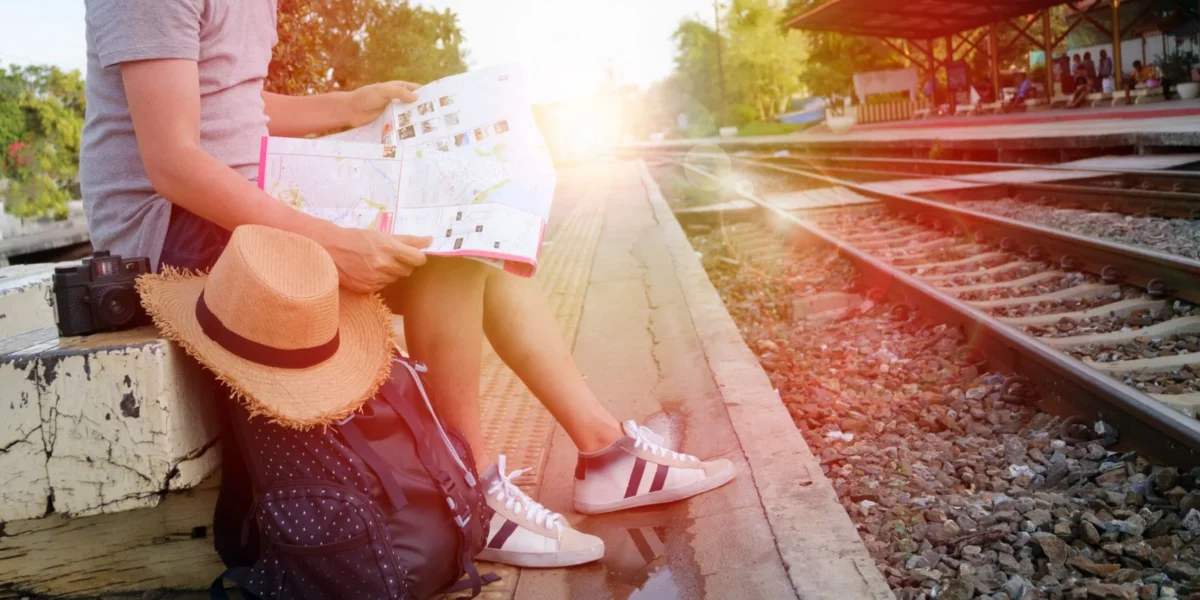 Person sitting at train station platform reading map, embracing travel adventure.