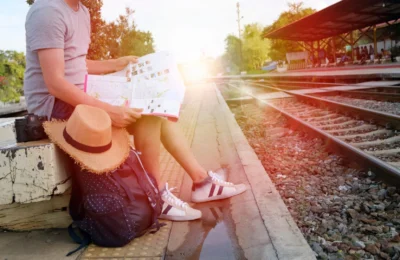 Person sitting at train station platform reading map, embracing travel adventure.