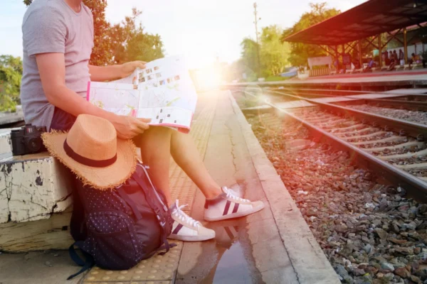 Person sitting at train station platform reading map, embracing travel adventure.