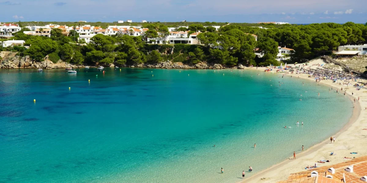 A stunning view of a beach in Menorca with clear waters and lush greenery.