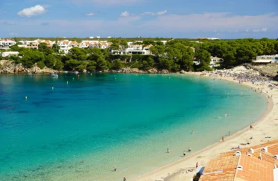 A stunning view of a beach in Menorca with clear waters and lush greenery.
