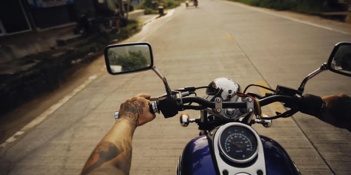 Tattooed arms controlling a motorcycle on a scenic open road, capturing adventure and freedom.