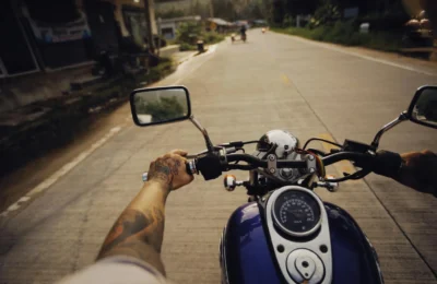 Tattooed arms controlling a motorcycle on a scenic open road, capturing adventure and freedom.