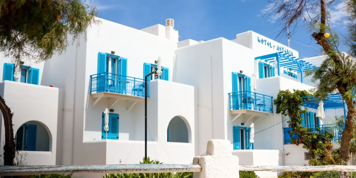 Whitewashed Greek hotel with blue shutters in Naxos under a clear sky.