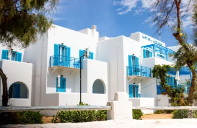 Whitewashed Greek hotel with blue shutters in Naxos under a clear sky.