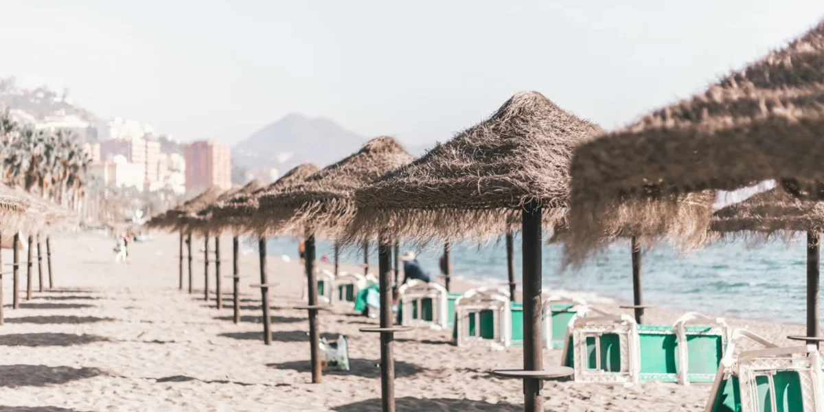 A serene sandy beach with straw umbrellas and clear skies, perfect for a summer vacation in Malaga, Spain.