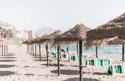 A serene sandy beach with straw umbrellas and clear skies, perfect for a summer vacation in Malaga, Spain.