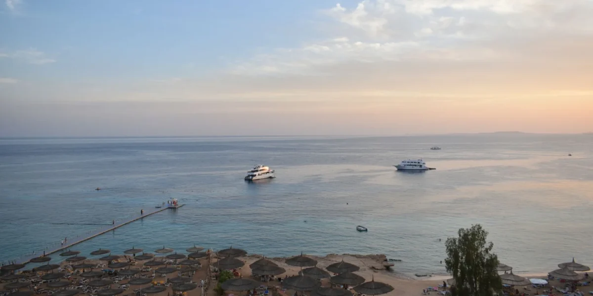 Stunning aerial view of Sharm El Sheikh's beach and sea during sunset with boats and parasols.