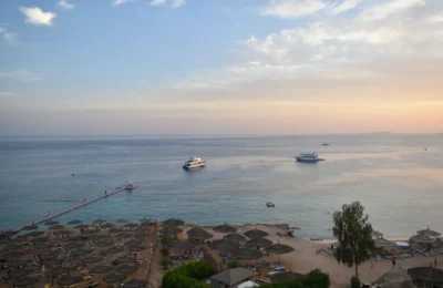 Stunning aerial view of Sharm El Sheikh's beach and sea during sunset with boats and parasols.