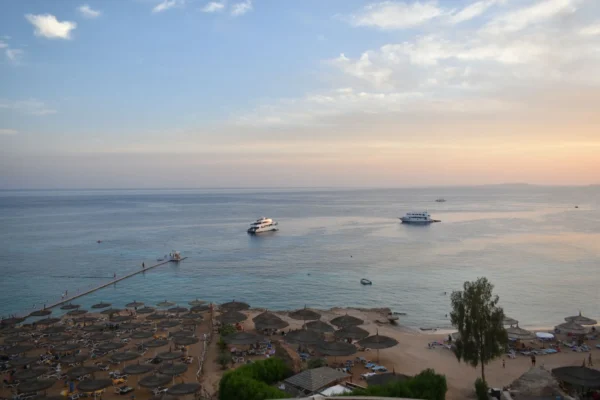 Stunning aerial view of Sharm El Sheikh's beach and sea during sunset with boats and parasols.